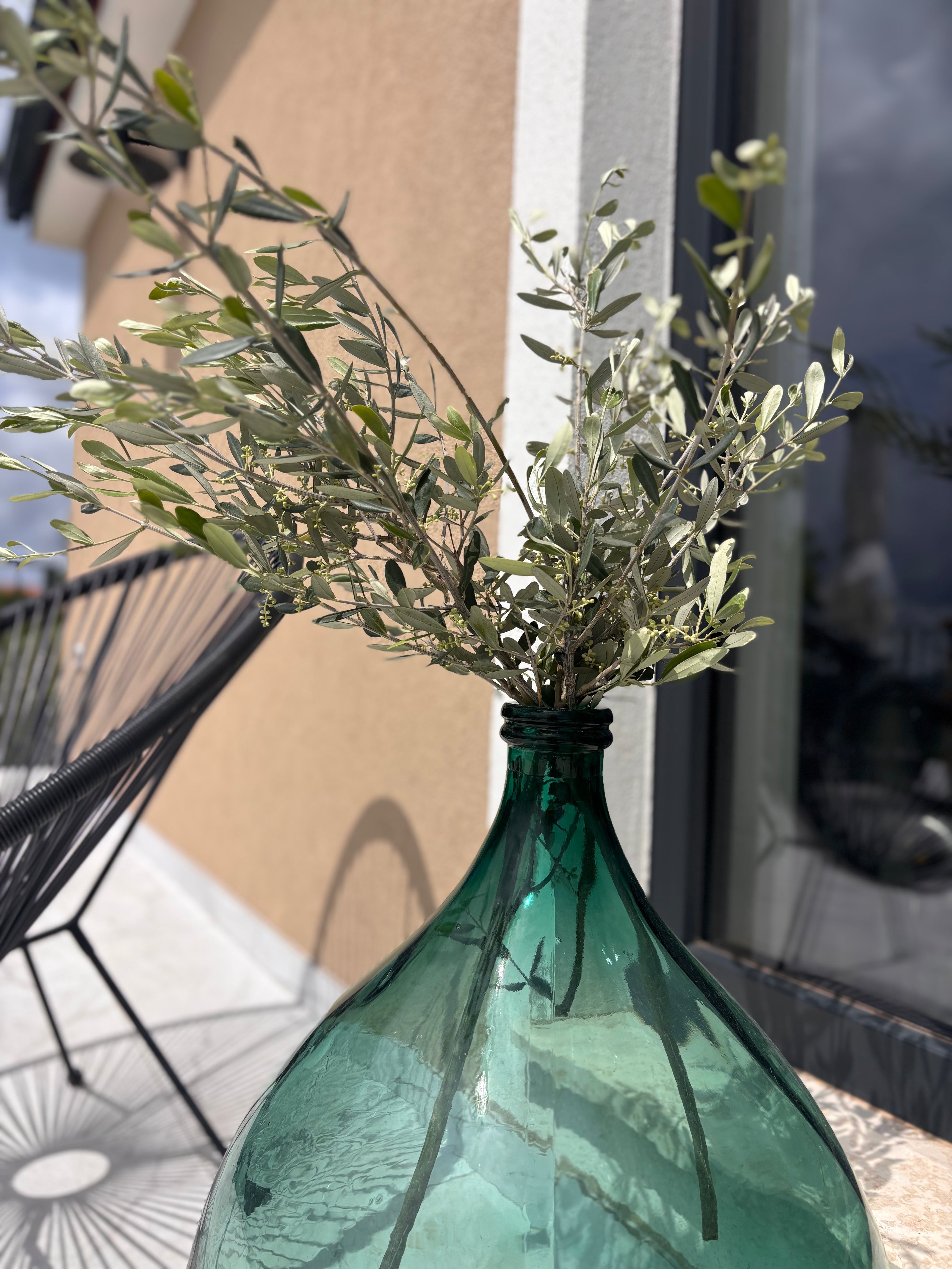 Green glass bottle with olive branches against a blurred outdoor background