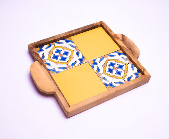 A square ceramic tray with geometric patterns, featuring a mix of yellow, blue, and multicolored tiles, placed on a wooden surface.